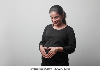 Young woman expecting a baby affectionately touches her tummy - Shutterstock ID 2102776378