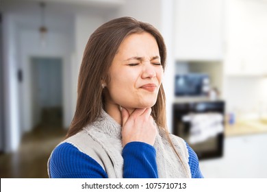 Young woman experiencing strong throat ache because of flu cold as swallowing discomfort expression concept on indoor room background