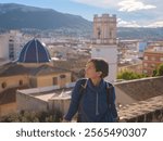 Young woman exploring historic castle in Denia, Alicante province, Spain, scenic views of town below, set against cooler season backdrop. blend of history and tranquility in timeless setting.