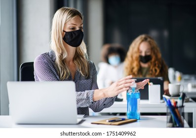 Young Woman With Face Mask Back At Work In Office After Lockdown, Disinfecting Hands.