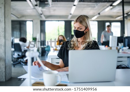 Young woman with face mask back at work in office after lockdown, working.