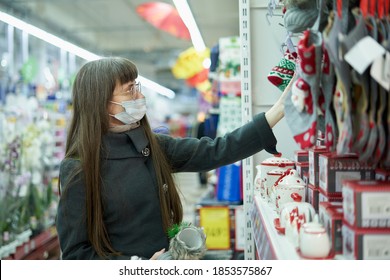 Young Woman In Face Mask Chooses Christmas Items On The Shelf In The Store For Shopping