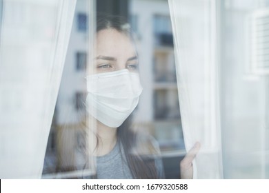 Young Woman in Face Mask Looking out the Window. Staying Home in Quarantine. - Powered by Shutterstock