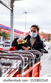 Young Woman With Face Mask Using Hydroalcoholic Gel Before Taking Shopping Cart,. New Normal Retail Shopping Concept