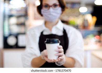 Young Woman With Face Mask Working Indoors In Coffee Shop, Holding Coffee.