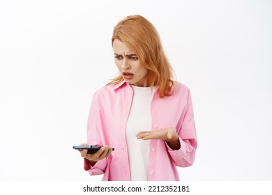 Young Woman Facing Problem On Mobile Phone, Looking Frustrated And Upset At Smartphone, Standing Over White Background