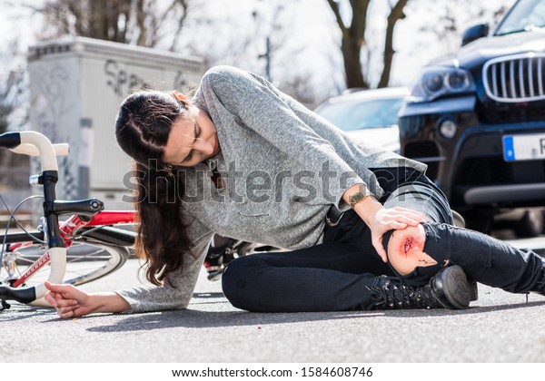 Young woman fallen down on the ground with a\
bleeding scrape on the knee after severe injury in bicycle accident\
on the street