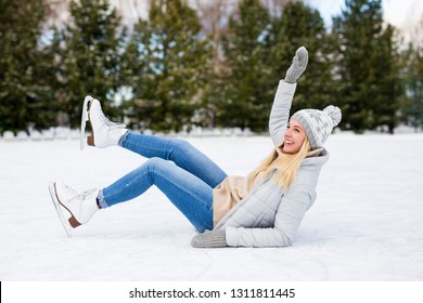 Young Woman Falling Down While Ice Skating At Winter Rink