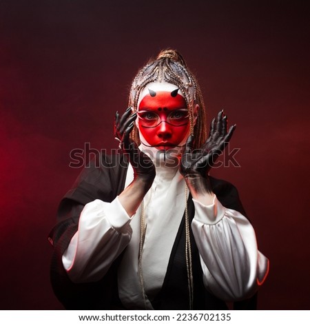 A young woman in fantastic makeup and an Asian kimono, the image of a cyber geisha. dancing on a dark background with red backlight