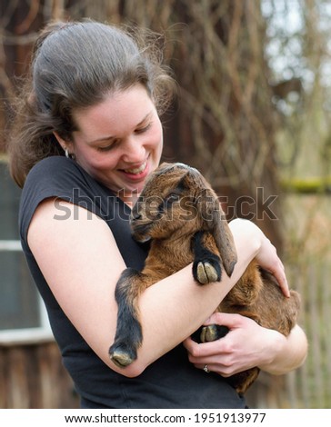 Young woman farmer with adorable baby goat in the arms (Capra aegagrus hircus)