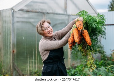 young woman farmer harvesting carrots from the soil - Powered by Shutterstock