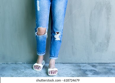 Young woman fashion with ripped jeans and flip flop with concrete wall in background