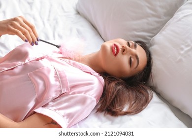 Young woman with feather stick lying on bed