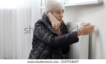 Young woman feeling cold at home calling repairman to fix broken heating radiator. Concept of energy crisis, high bills, broken heating system, economy and saving money on monthly utility payments.