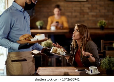 Young woman feeling dissatisfied about her order and arguing with a waiter in a restaurant. 