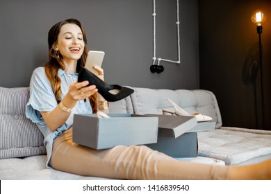 Young Woman Feeling Excited With A New Shoes, Unpacking Purchases And Taking Photo With Phone At Home