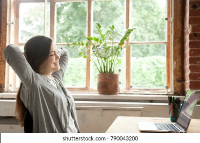 Young woman feeling happy relaxed sitting at desk with laptop, smiling freelancer enjoys distance online job stretching at home workplace, motivated girl satisfied with good news or having work break