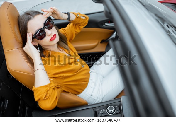 Young woman feeling\
headache while sitting on the driver\'s seat of convertible car.\
View from above