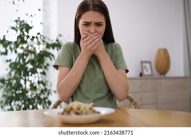 Young Woman Feeling Nausea While Seeing Food At Wooden Table Indoors