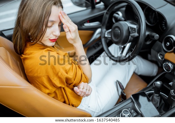 Young woman feeling\
stressed, having a headache while sitting on the driver\'s seat of\
convertible car