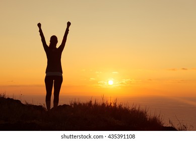 Young woman feeling victorious facing the beautiful sunset. 