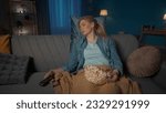 The young woman fell asleep during the film. A tired woman sleeps, sitting on the couch close up, with popcorn on her lap, and with a remote control in her hand. Boring film.