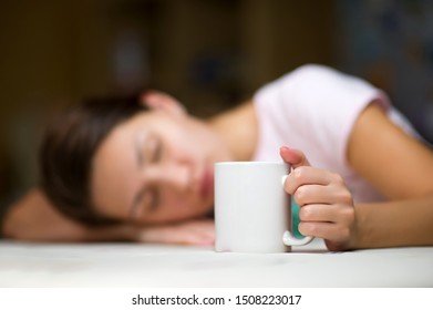 young woman fell asleep at the table holding a white mug of coffee