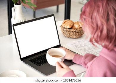 Young Woman, Female Student Sitting At Kitchen Table At Home Using Laptop Computer With Mock Up White Screen For Ads, Drinking Coffee. Over Shoulder Close Up View.