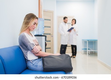 Young woman filling nervous sitting at hospital corridor waiting while two doctors talking on a backgroud