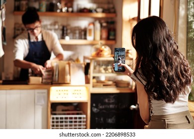 Young woman filming coffeeshop worker packing orders in paper bags