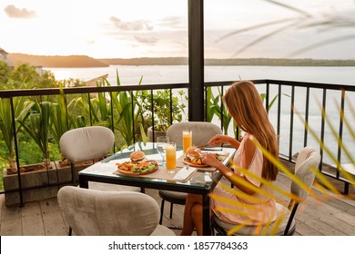 Young Woman In A Fine Dining Restaurant Eat A Hamburger With Salad And French Fries, Enioy Sunset By The Sea