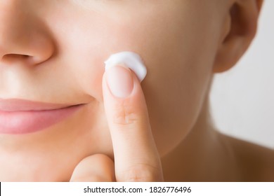 Young woman finger applying white moisturizing cream on cheek. Care about clean and soft face skin. Daily beauty product. Closeup.