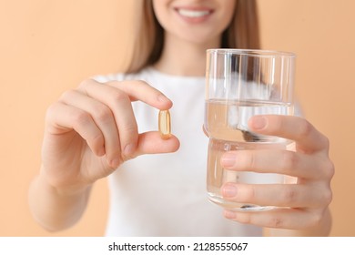 Young woman with fish oil pill and glass of water on color background, closeup - Shutterstock ID 2128555067