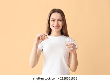 Young Woman With Fish Oil Pill And Glass Of Water On Color Background