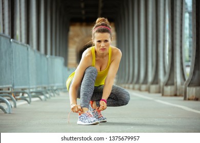 Young Woman In Fitness Clothes On Pont De Bir-Hakeim Bridge In Paris Tying Shoelaces.