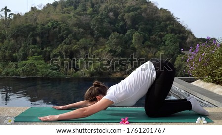 Young woman in fitness uniform doing stretching near the pool outdoors.