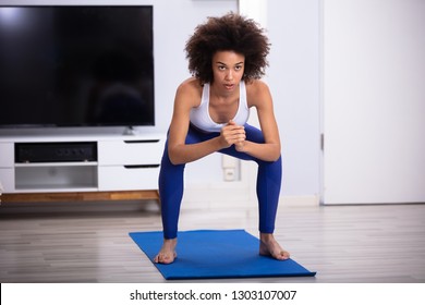 Young Woman In Fitness Wear Doing Squat Exercise At Home