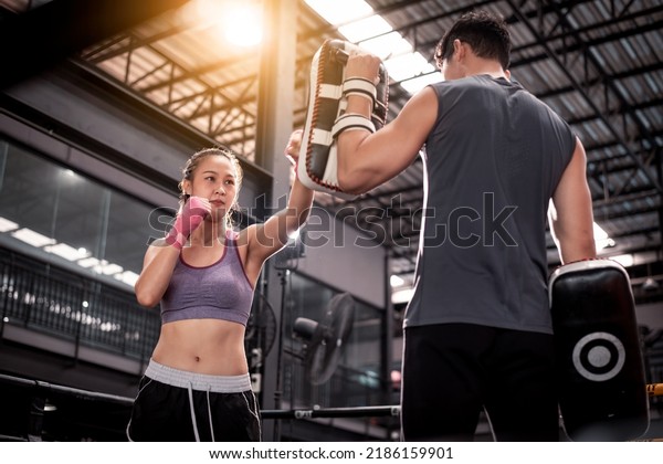 Young woman fitness wearing hand bandage ready\
to boxing throw a punch with trainer couple lover holding pads for\
boxing session ,they exercise for strong make muscle and good\
healthy lifestyle.