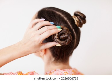 A young woman fixes her hair bun  She wears rainbow gradient man