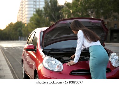 Young woman fixing broken car on city street