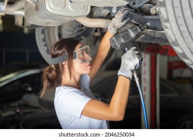 A young woman fixing the underbody of a car with a  impact wrench in a garage. - Powered by Shutterstock