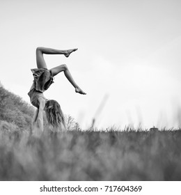 Young Woman With Flexible Body Doing Somersault On Spring Green Grass