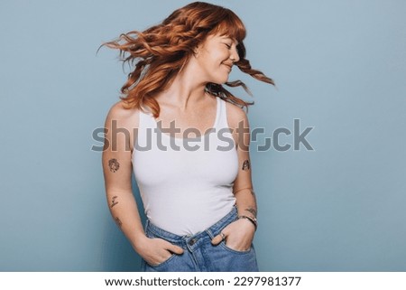 Young woman flipping her ginger hair while standing in a studio. Happy young woman having fun in a tank top and jeans.