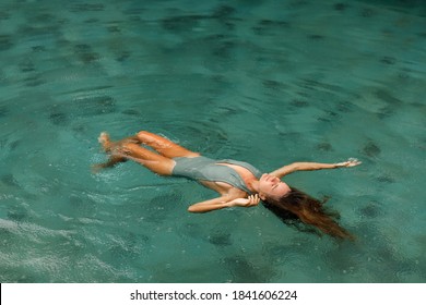Young woman floating on the back in the simming pool under the rain drops