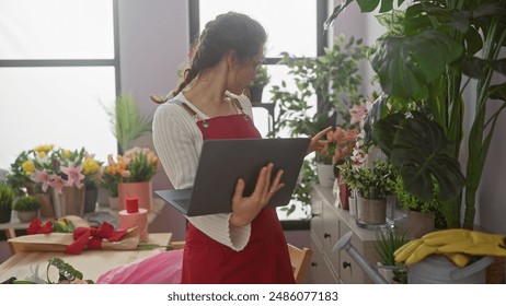 A young woman florist in a red apron uses a laptop among varied houseplants within a cozy flower shop interior. - Powered by Shutterstock