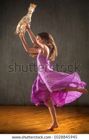 Young woman in flowing lavender dress raising overhead an antique carousel horse in the studio.