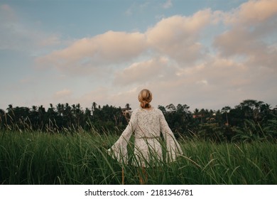 Young woman in flown white dress walking through tall grass field