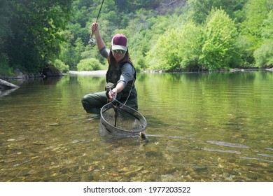 Young Woman Fly Fishing And Catching A Brown Trout