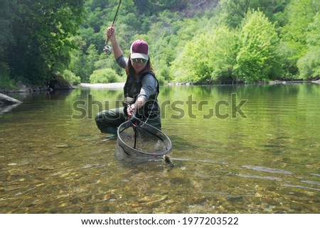 young woman fly fishing and catching a brown trout