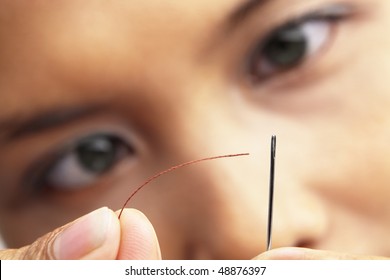 A Young Woman Focus To Put The Sewing Thread Into Needle